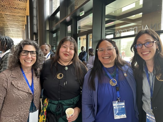 Faith and three women smiling and wearing participant lanyards at the Women in Water Data Diplomacy Symposium.