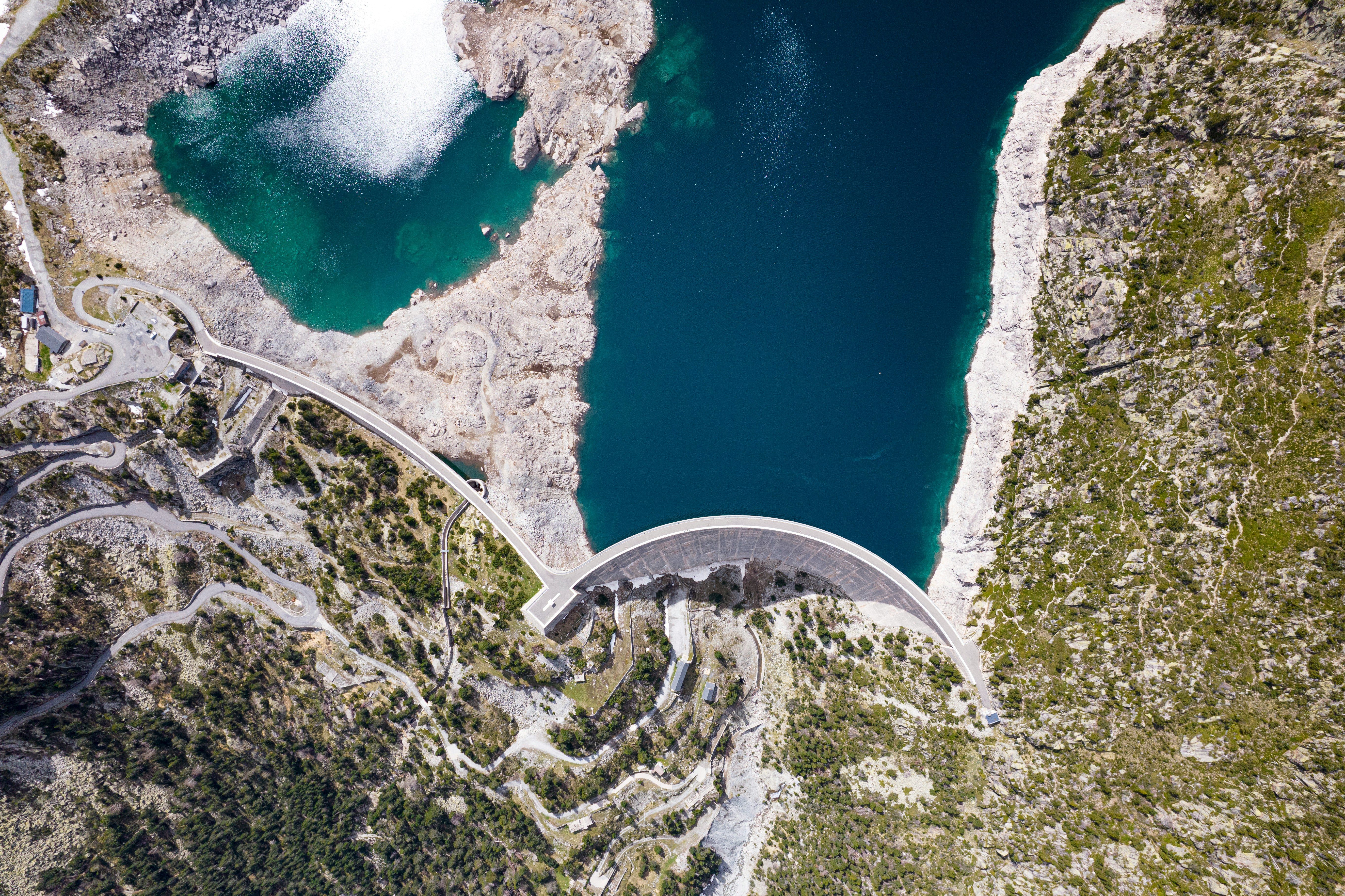 An aerial view of blue water in a dam surrounded by sparsely forested hills.
