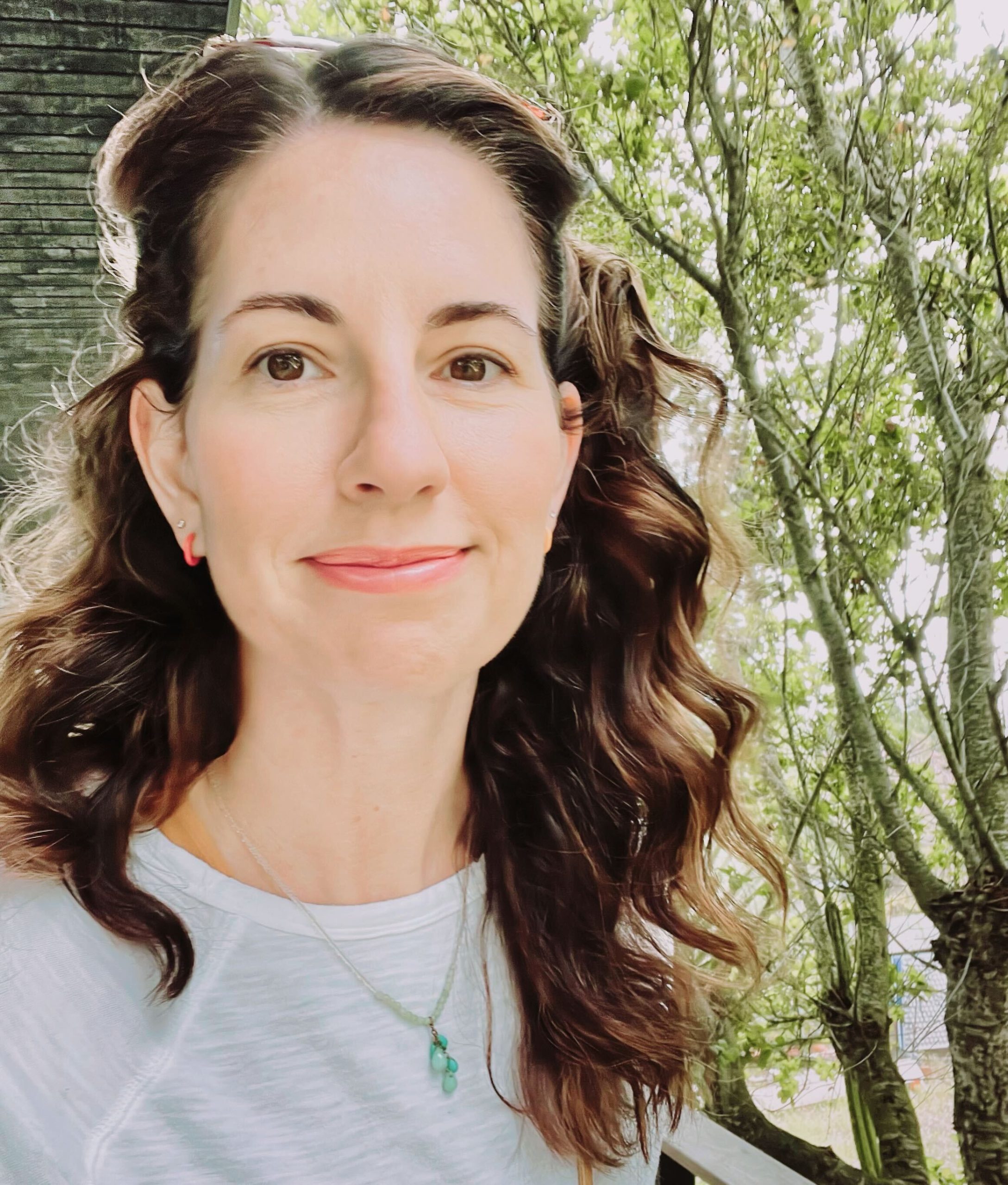 A headshot of Sara Larsen, a woman with long brown hair staring straight into the camera with trees in the background.